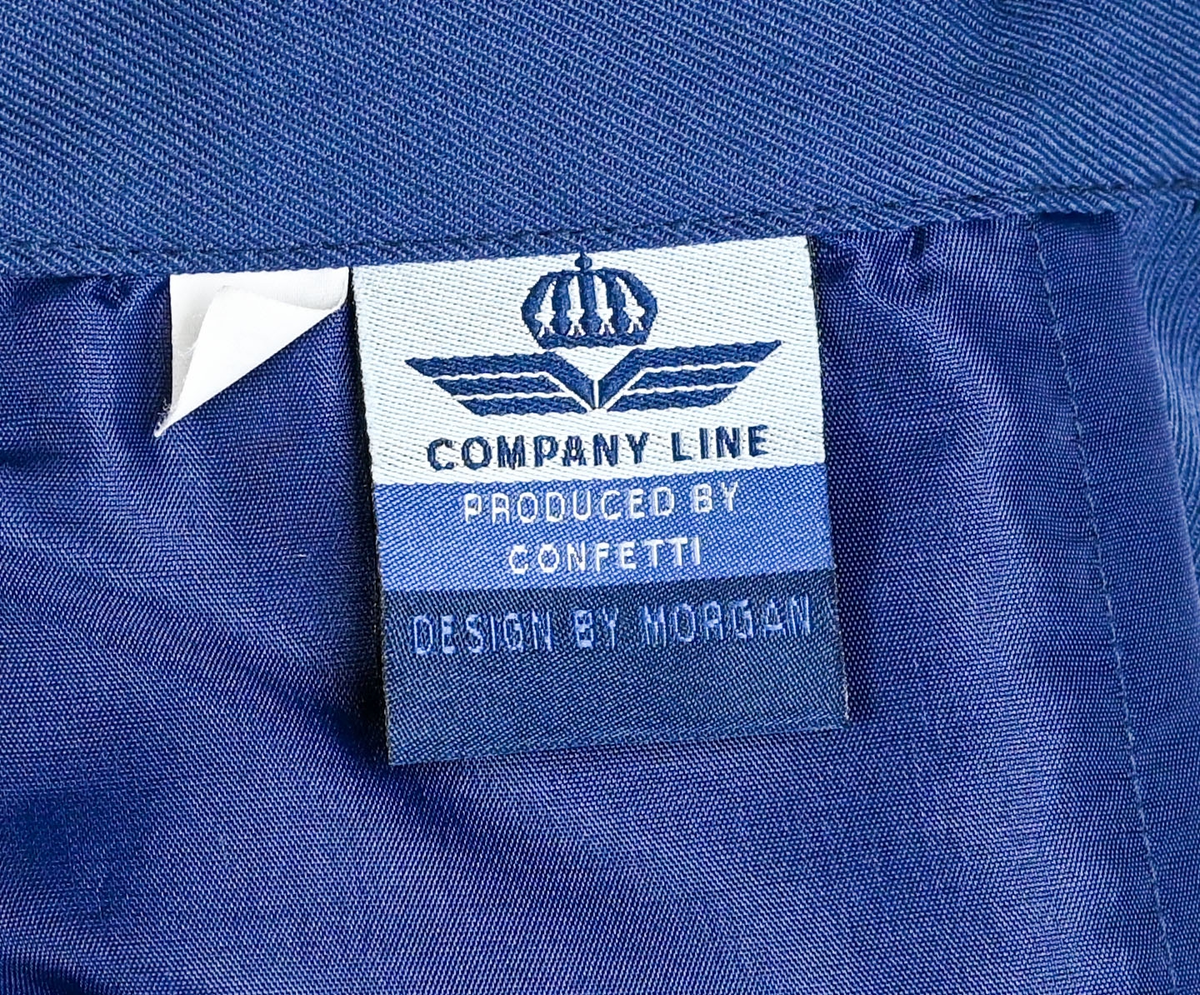 Kjol i mörkblå textil till ämbetsdräkt för kvinnlig personal vid Luftfartverket. Kjolen har två enkla framfickor. Längs midjan sitter fyra hällor för bälte. I bak i plaggets nederkant finns ett gångveck. Kjolen stängs i bak med dragkedja och knapp. Fodringen är mörkblå. 

På insidan i bak sitter två lappar med information om tillverkare och storlek. På ena lappen finns även Luftfartsverkets logga. Kjolen är producerad av Confetti i storlek C40. I en av hällorna sitter en papperslapp med nummer 8632. På denna har texten 3/10 påförts i bläck.
