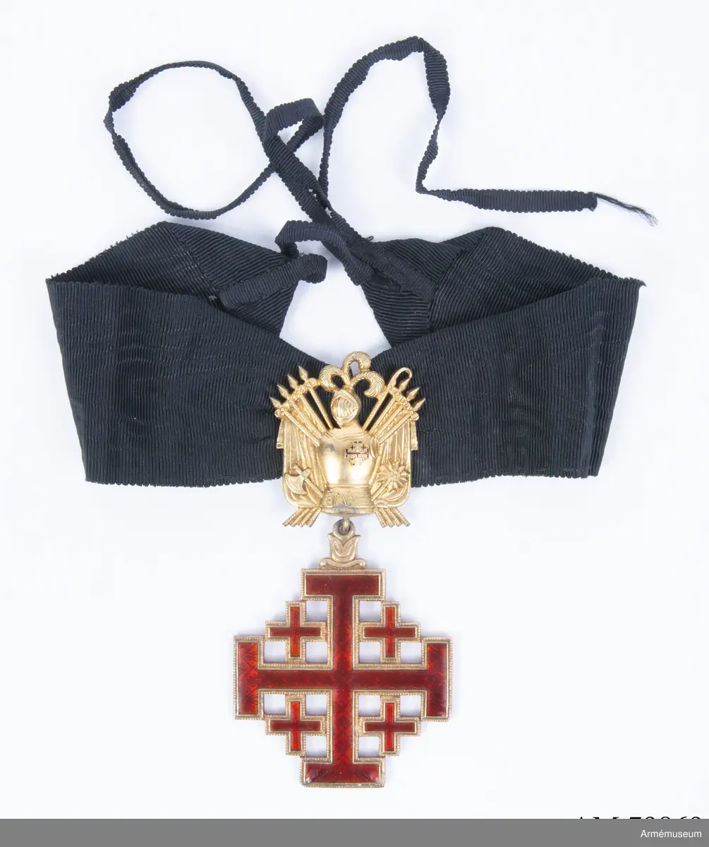 Påvliga Heliga Gravens orden, kommendörstecken i svart band. 
Miniatyr och knapp. Ordenstecknet i form av pilgrimssnäcka tilldelades ordensriddare som genomfört en pilgrimsresa till det heliga landet.

Förvaras i samhörande etui.