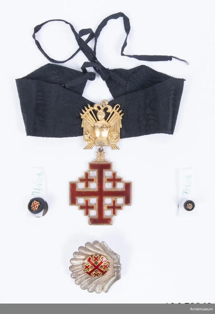 Påvliga Heliga Gravens orden, kommendörstecken i svart band. 
Miniatyr och knapp. Ordenstecknet i form av pilgrimssnäcka tilldelades ordensriddare som genomfört en pilgrimsresa till det heliga landet.

Förvaras i samhörande etui.