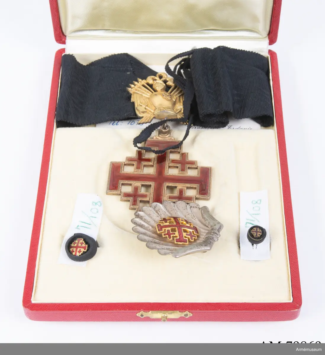 Påvliga Heliga Gravens orden, kommendörstecken i svart band. 
Miniatyr och knapp. Ordenstecknet i form av pilgrimssnäcka tilldelades ordensriddare som genomfört en pilgrimsresa till det heliga landet.

Förvaras i samhörande etui.