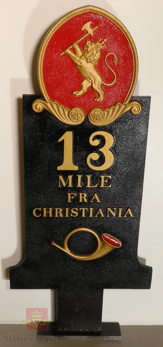 Flerfarget støpejernstavle med riksvåpen, posthorn og teksten "13 MILE FRA CHRISTIANIA"
Plata har vært oppusset og malt om.