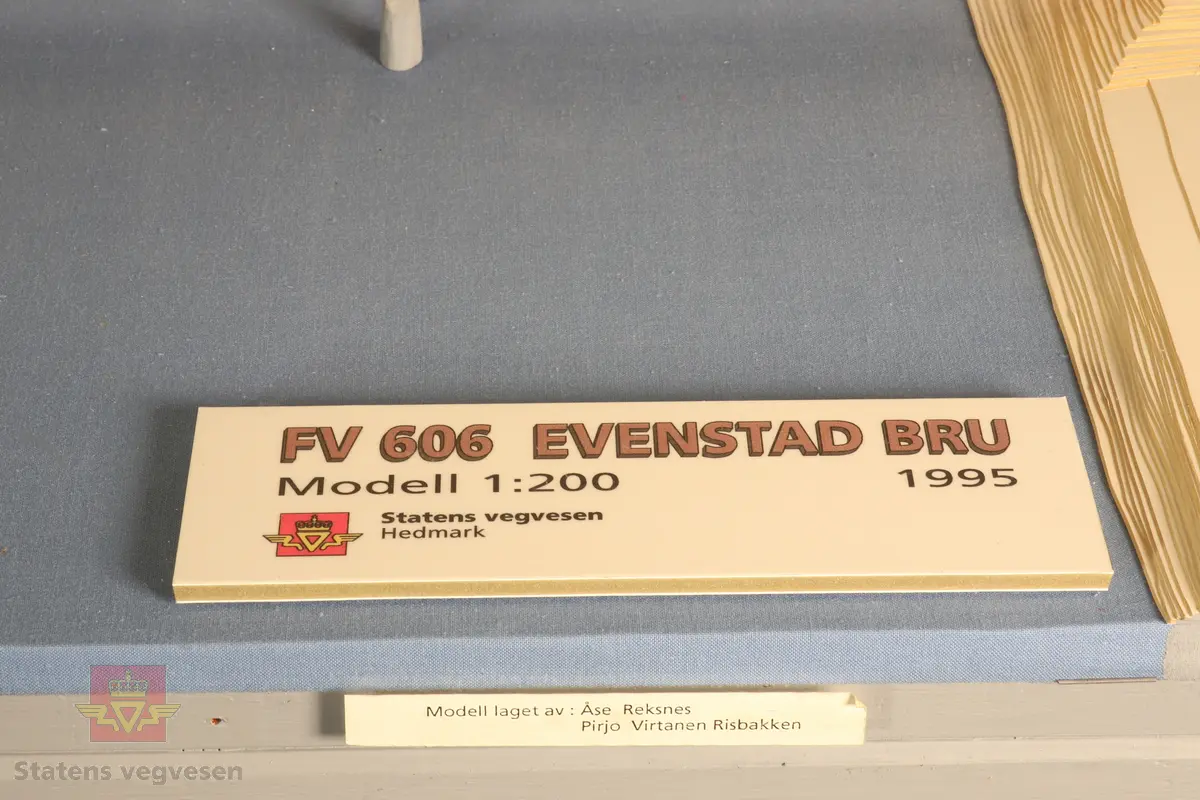 Miniatyr bru i målestokk 1:200. Laget av papir, tre og metall. Står i monter laget av tre og plast.