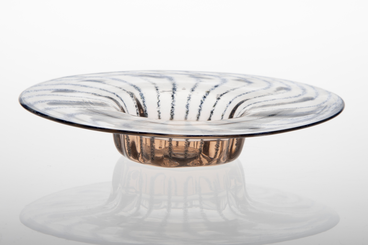 En av tre skåler i klart glass. Skålene har tjukk bunn med smal diameter. Opphøyet fra bunnen har skålene brede kanter. Kantene er dekorert med blå striper som slynger seg ut fra midten.