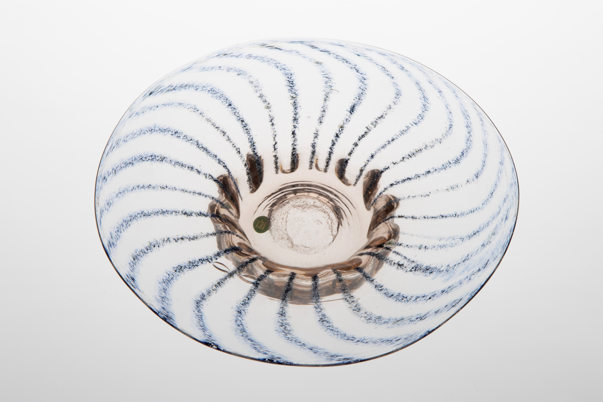 En av tre skåler i klart glass. Skålene har tjukk bunn med smal diameter. Opphøyet fra bunnen har skålene brede kanter. Kantene er dekorert med blå striper som slynger seg ut fra midten.