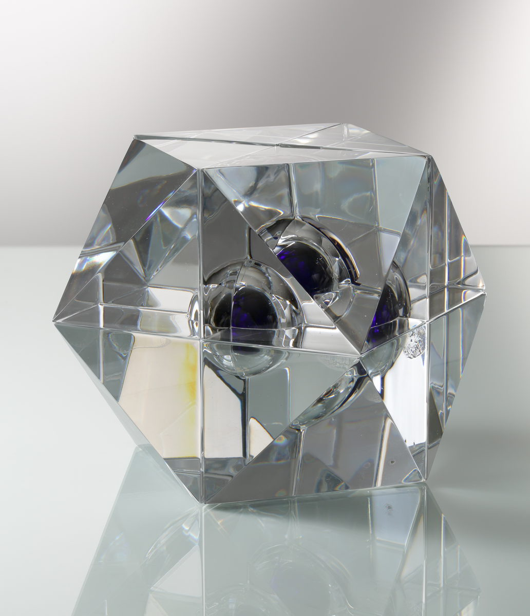 Formgivare: Jan Johansson. Skulptur i massivt klarglas, sjudelad geometrisk form med kula i blåtonat glas.