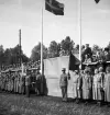 Kung Gustaf V:s besök i Liatorp 1939. 
Kungen hälsar de församlade från en tribun. Något bakom honom skymtar landshövdingen i Växjö, August Beskow. Nedanför står  bl a en mängd lottor och militärer. 

Gustaf V (1858-1950), reg. 1907-1950. 
August Beskow (1882-1946), landshövding i Kronobergs län 1925-1944.