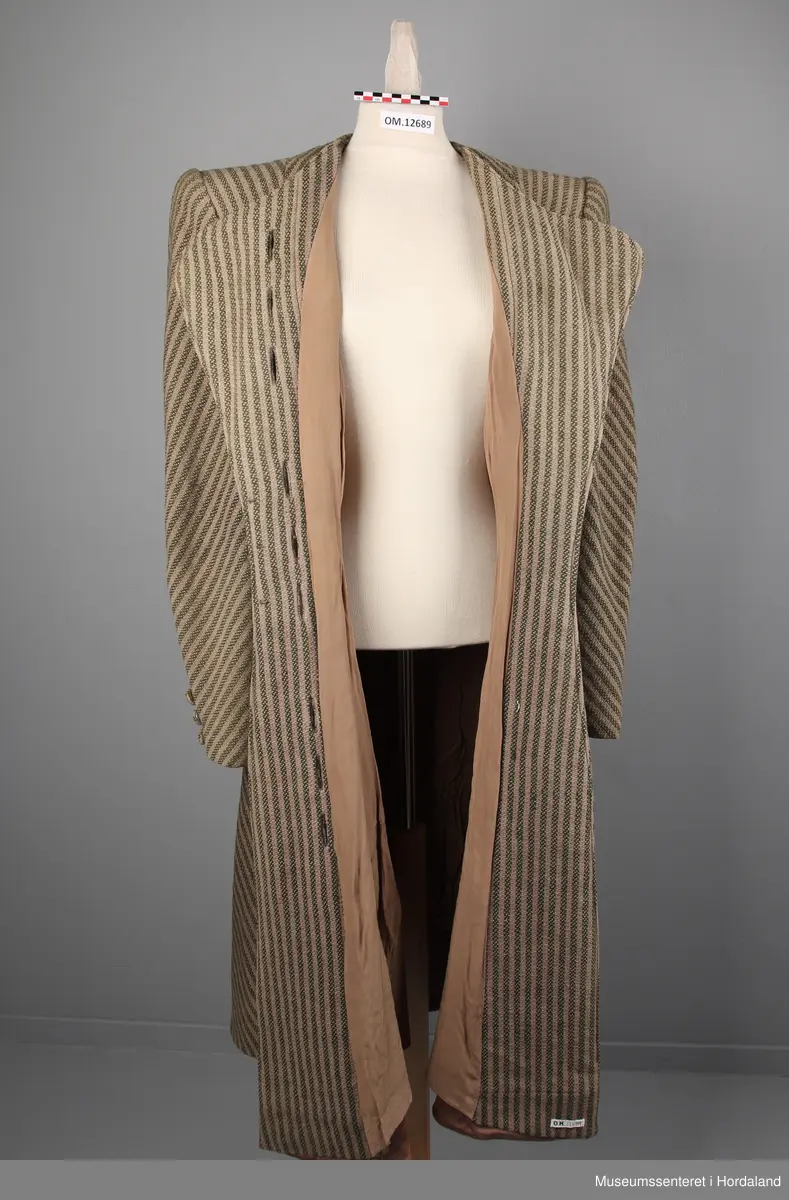 Kåpa er sydd saman av 10 bredder (skråklipte), der alle stripene møtes rett i alle saumane. Fasongsydd og sterkt innsvinga i livet. Slag, men ikkje krage. Trekte knappar - 9 stk i same stoff som kåpa. Knapphola ligg i ein saum - altså ikkje klipte opp og sydde. To stikklommer på kvar side framme i saumen. Tre trekte knappar framme på ermene. Fora med kunstsilkestoff. På innsida nede har kåpa skoning (forsterking). Store skulderputer.