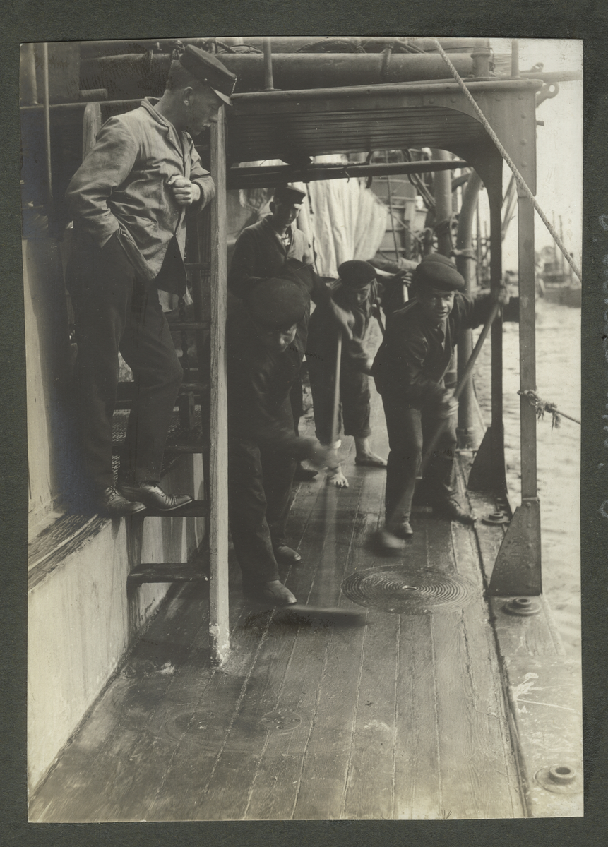 Män fyller på olja (ubåten Hvalen) vid kaj under ubåtsskolan 1911. Alla bär arbetskläder och vegamössa. Runt omkring på kajen syns oljetunnor.