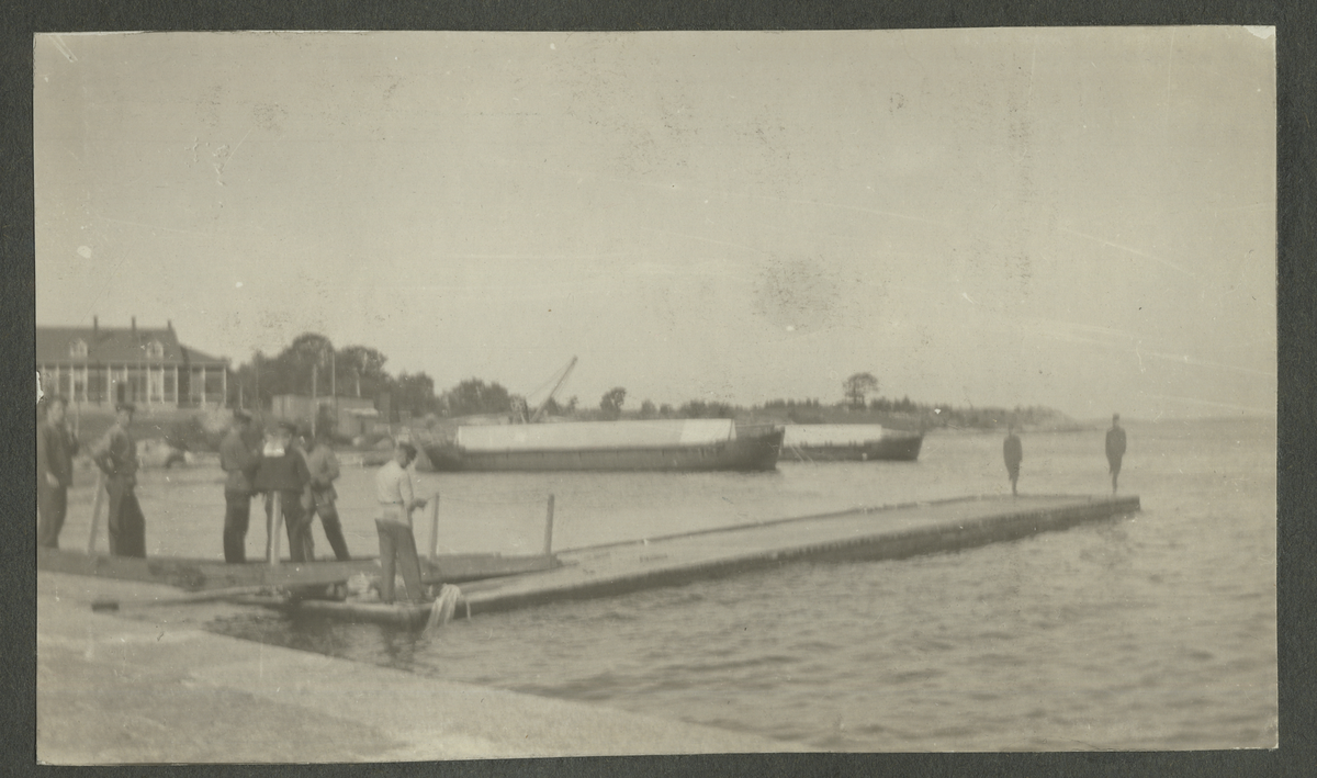 Karlskrona 1914. Foto på undervattensbåten Nr: 4 förtöjd vid brygga. På ubåten och kajen står några sjömän. I bakgrunden syns byggnader under uppbyggnad.