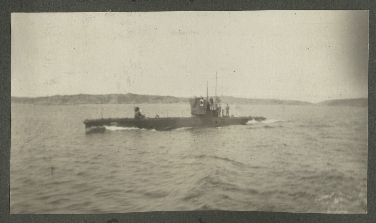 Undervattensbåten nr. 3 över ytan 1916 på Västkusten. På däck står ett antal sjömän samt en matros med vit hatt som böjer sig ned. Flaggan vajar i fören.