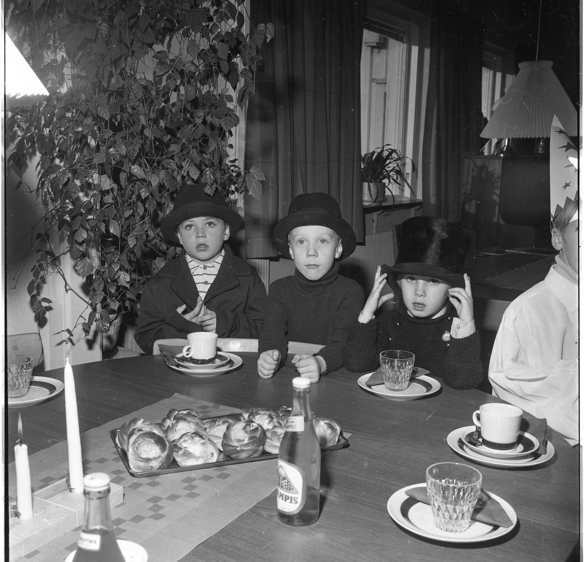 Tre små pojkar med hatt, och en stjärngosse sitter vid ett bord med läsk och bullar.