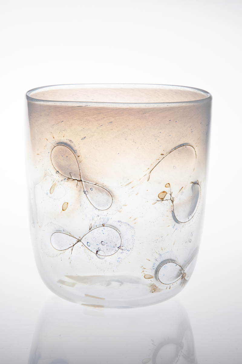 Sylinderformet glassbolle. Bunn og nedre del av korpus er utført i klart glass, mens øvre del domineres av melkehvitt halvgjennomskinnelig glass. Innlagte metalltråder danner åttetalls- og halvsirkelformede elementer på korpus. I glasset er det en rekke luftblærer i ulike størrelser, samt dråpeformede spetter i blått og brunt. Puntemerke under bollens bunn.