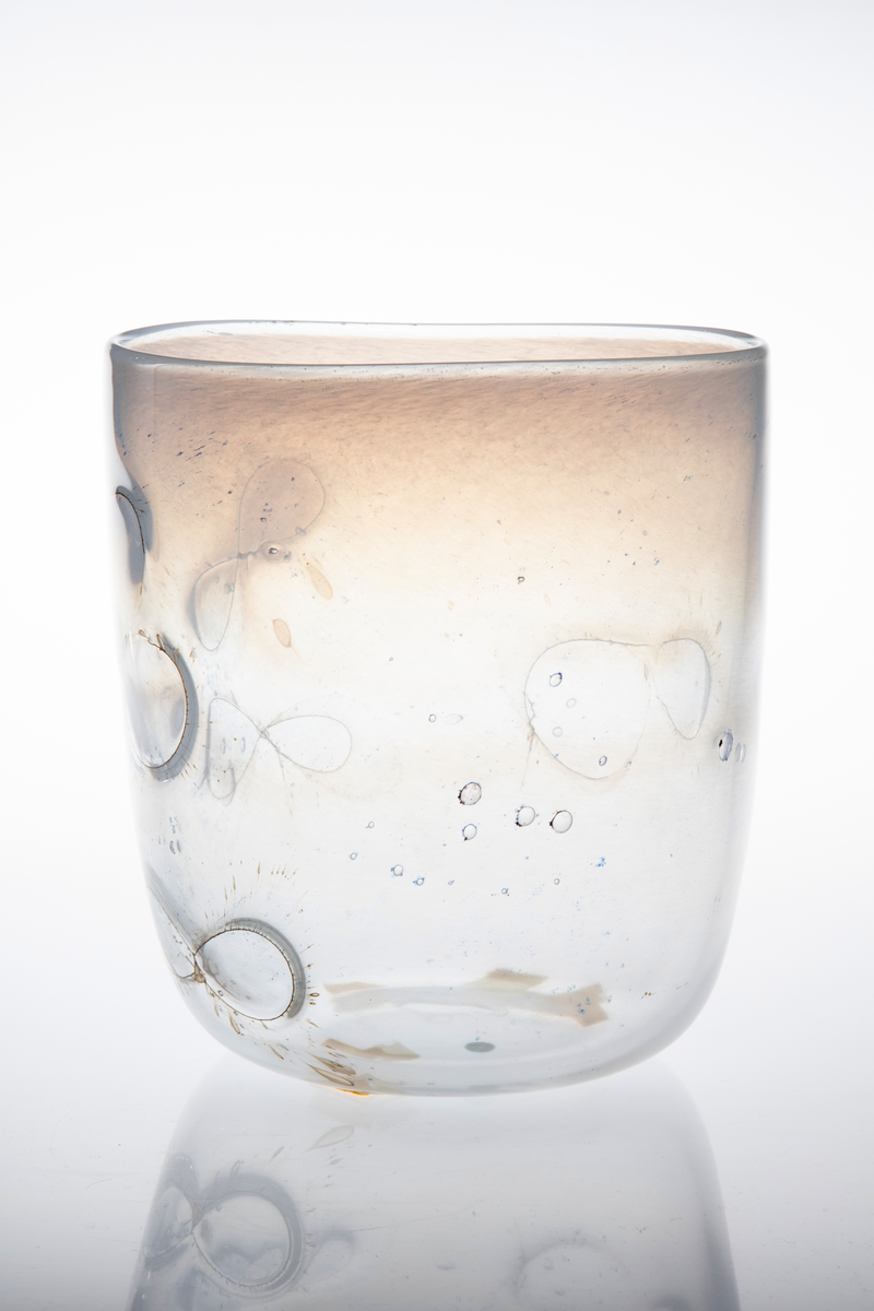 Sylinderformet glassbolle. Bunn og nedre del av korpus er utført i klart glass, mens øvre del domineres av melkehvitt halvgjennomskinnelig glass. Innlagte metalltråder danner åttetalls- og halvsirkelformede elementer på korpus. I glasset er det en rekke luftblærer i ulike størrelser, samt dråpeformede spetter i blått og brunt. Puntemerke under bollens bunn.