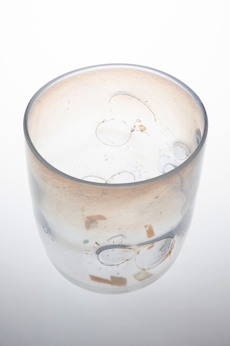 Sylinderformet glassbolle. Bunn og nedre del av korpus er utført i klart glass, mens øvre del domineres av melkehvitt halvgjennomskinnelig glass. Innlagte metalltråder danner åttetalls- og halvsirkelformede elementer på korpus. I glasset er det en rekke luftblærer i ulike størrelser, samt dråpeformede spetter i blått og brunt. Puntemerke under bollens bunn.