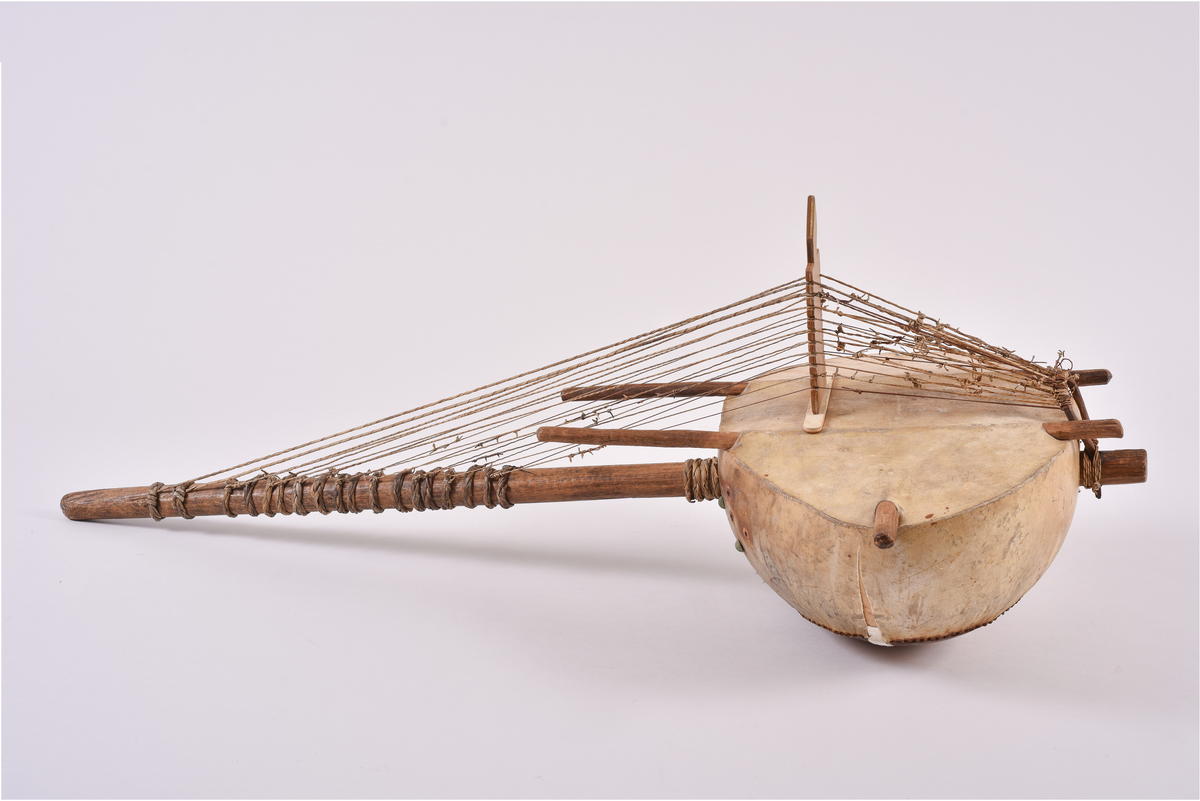 Harpe bestående av en kalebass trukket med skinn. Strenger festet i en lang pinne i tre, trukket i spenn over en bru over kalebassen og festet i ring av metall i enden. Skinnet festet med nagler av metall.