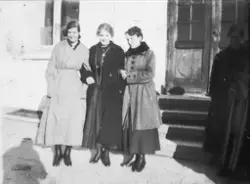 Tre kvinner i kåper, stående utenfor bygning.