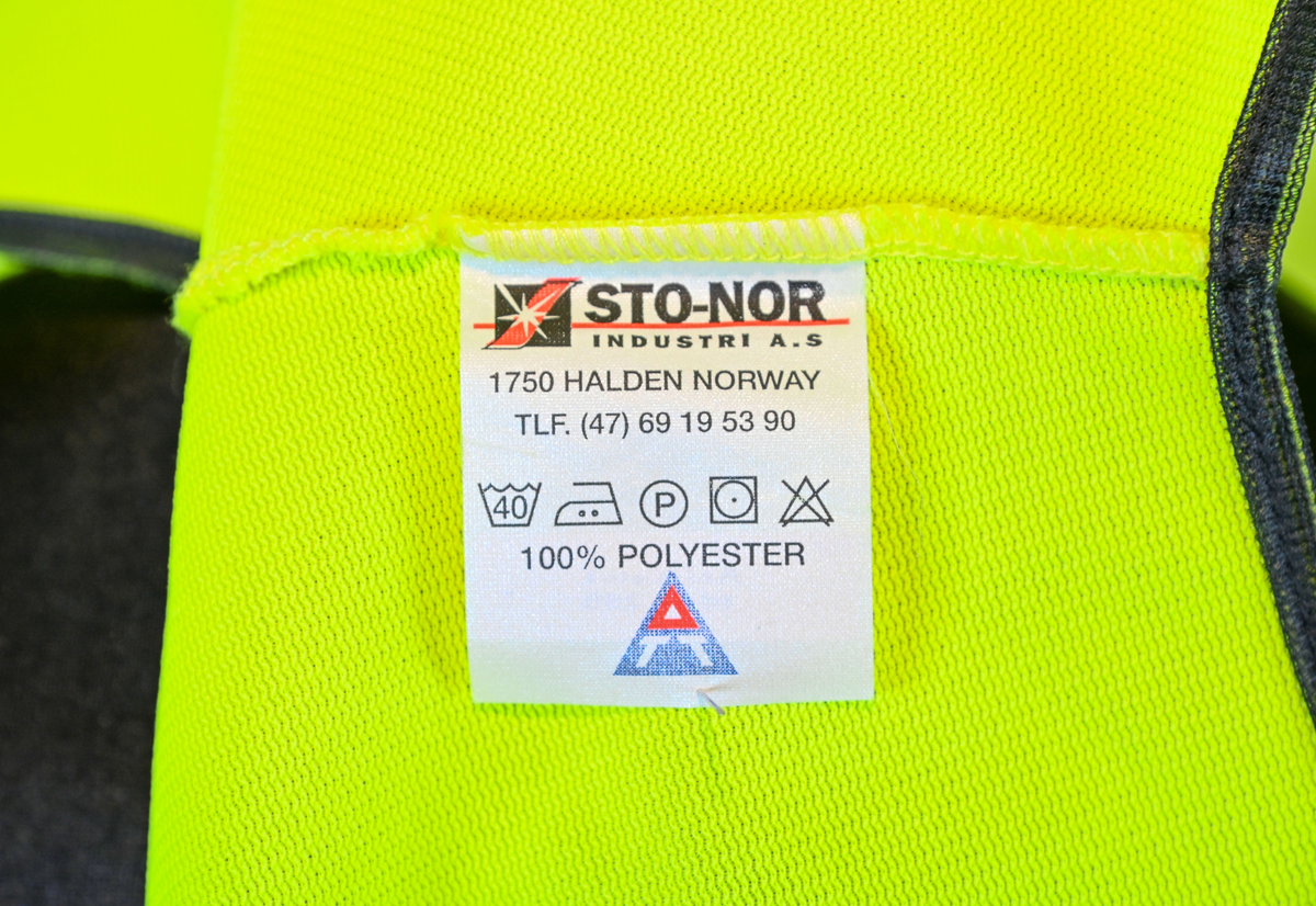 Gul reflexväst för banpersonal. Västen har två breda reflexband som går hela vägen runt och stängs framtill med kardborreband. På vänster sida om öppningen sitter en ficka och ovanför den en ögla i samma tyg som västen. Svart passpoal vid alla kantsömmar. På insidan vid vänster axel sitter en produktionsetikett med tvättråd och produktinformation.

Västen är tillverkad av Sto-Nor Industri A.S, Norge.