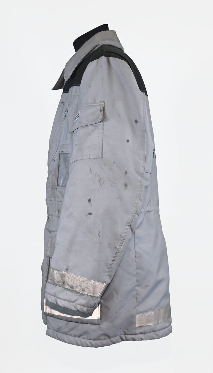 Grå varseljacka med svart foder tillhörande anställd på Luftfartsverket. Jackan har flera fickor som stängs med dragkedja eller kardborreband, samt en innerficka på vänster sida. Jackan är försedd med reflexer på båda ärmslut och båda framfickor. Luftfartsverkets logga sitte på höger bröst och ryggen. I jackan sitter en lapp med tvättanviselser. Jackan stängs med dragkedja i plast och sex stycken tryckknappar. Det finns även tryckknappar runt kragen för en eventuell luva som saknas. Jackan är väl använd och har flertalet smuts- och oljefläckar.

Jackan är i storlek L (54-56).