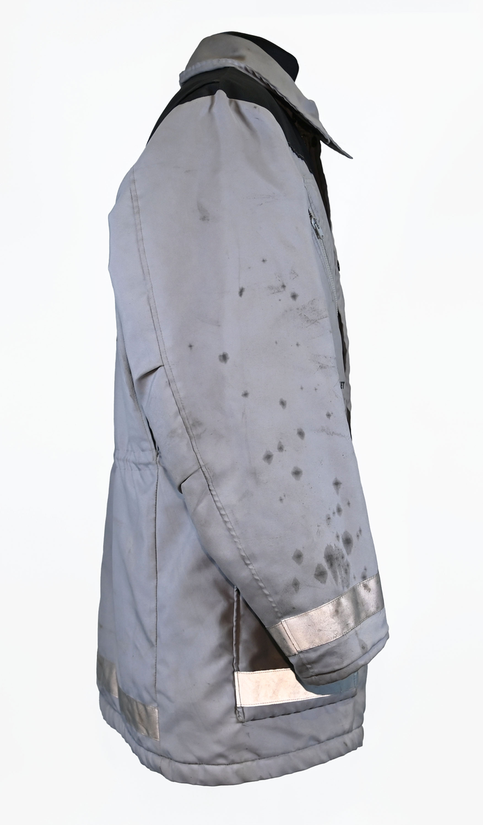 Grå varseljacka med svart foder tillhörande anställd på Luftfartsverket. Jackan har flera fickor som stängs med dragkedja eller kardborreband, samt en innerficka på vänster sida. Jackan är försedd med reflexer på båda ärmslut och båda framfickor. Luftfartsverkets logga sitte på höger bröst och ryggen. I jackan sitter en lapp med tvättanviselser. Jackan stängs med dragkedja i plast och sex stycken tryckknappar. Det finns även tryckknappar runt kragen för en eventuell luva som saknas. Jackan är väl använd och har flertalet smuts- och oljefläckar.

Jackan är i storlek L (54-56).