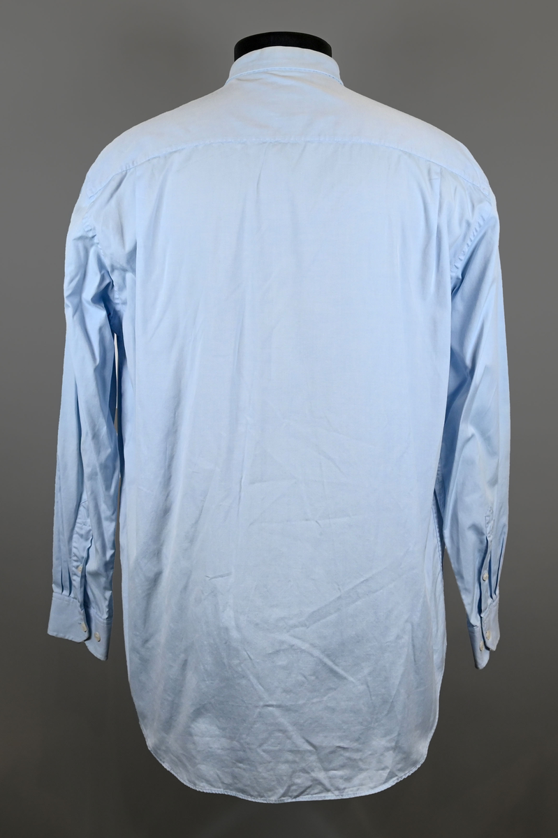 Blå långärmad skjorta som del av uniform från Luftfartsverket. Enkel knäppning med vita plastknappar och en bröstficka på vänster sida med Luftfartsverket logo broderad på. Vardera ärmslut har tre vita plastknappar vardera. I vänster innersöm titter en produktionsetikett med produktinformation och tvättråd. På etiketten är även två vita plastknappar i olika storlekar fastsydda.

Storlek L.