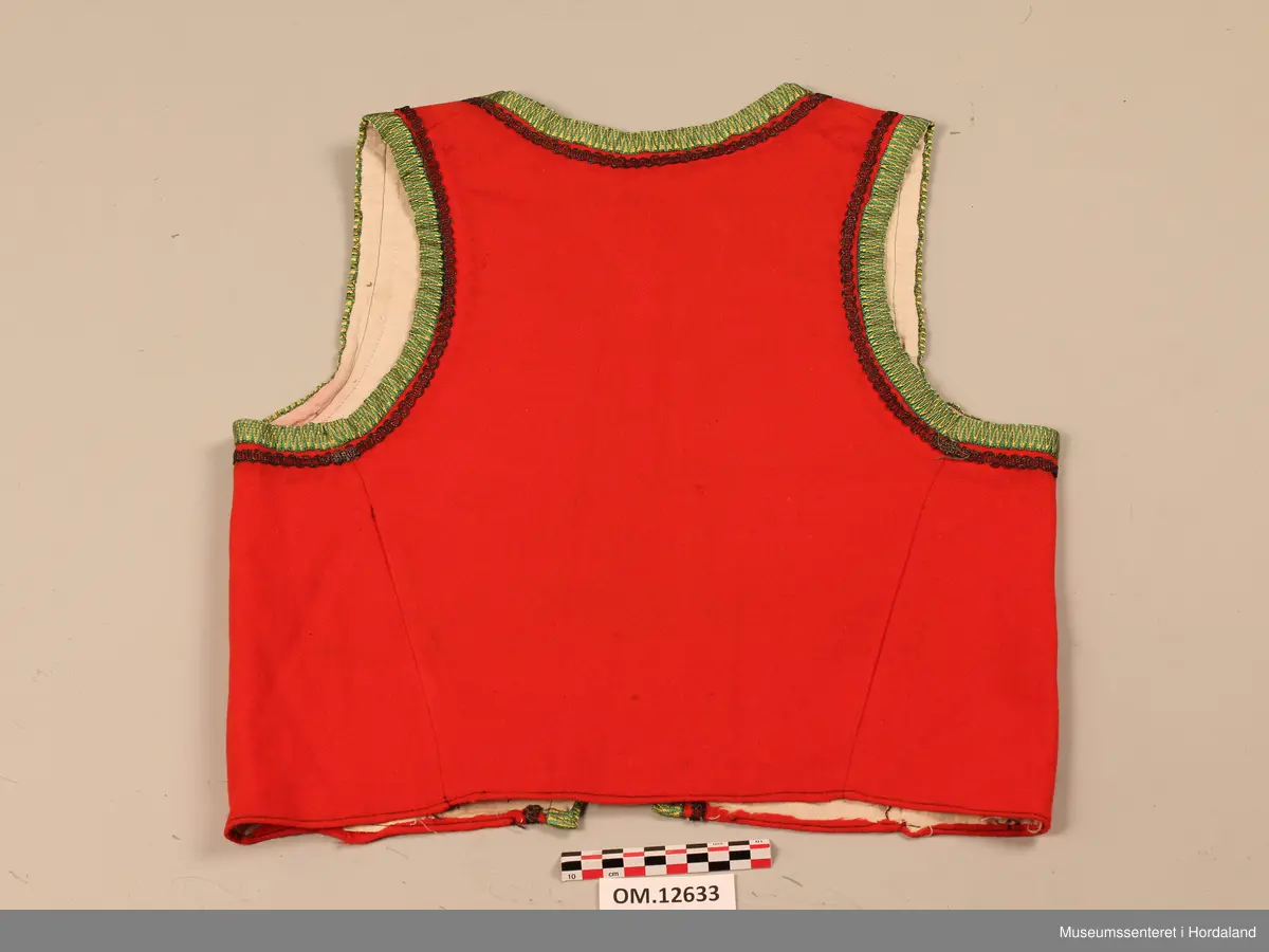 Raudt bunadsliv med grøne og gule silkekvardar (-band) rundt opningane. Innafor silkekvardane er det sydd på ei sølvsnor. Sidesaumane er trekte bakover (skrådde) på ryggen. Tre hekter i livet framme (kroker og maljer). På framstykket viser det at livet har hatt to innsnitt på kvar side tidligare. Sameleis kan ein sjå at her har vore påsydd tre borer på kvar side langs opninga framme. Det viser som svarte ringar på stoffet. Livet er nokså slitt og velbrukt. Både ullstoffet og bomullslerretet i livet er nokså tynt.