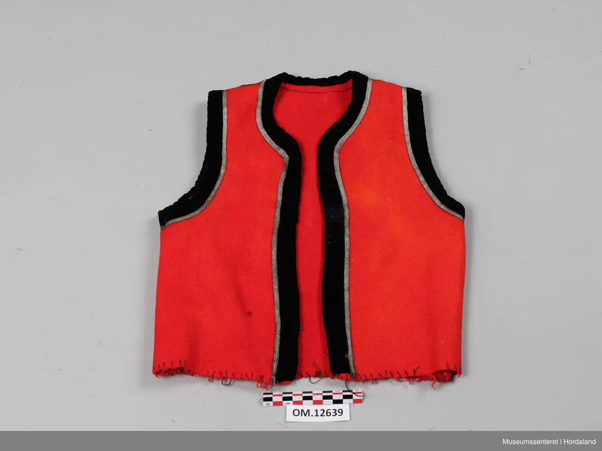 Raudt bunadsliv med kanting i svart fløyel. Innafor kantinga er det ei sølvsnor. To hekter i livet framme (kroker og maljer). Livet er ikkje fôra. Sidesaumane er trekte langt bak på ryggen, men i kvar side er livet sydd inn.