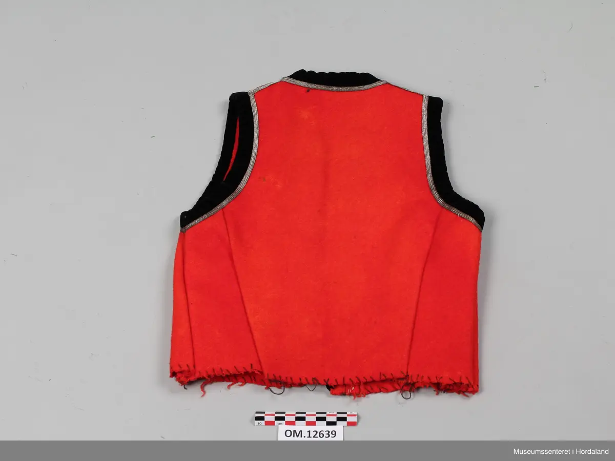 Raudt bunadsliv med kanting i svart fløyel. Innafor kantinga er det ei sølvsnor. To hekter i livet framme (kroker og maljer). Livet er ikkje fôra. Sidesaumane er trekte langt bak på ryggen, men i kvar side er livet sydd inn.