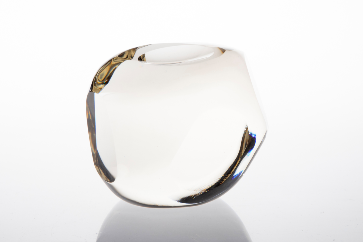 Irregulær kuleformet skulptur av massiv klart glass med slipte ovalformede og runde partier på yttersiden.