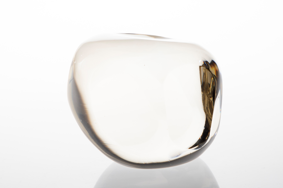 Irregulær kuleformet skulptur av massiv klart glass med slipte ovalformede og runde partier på yttersiden.