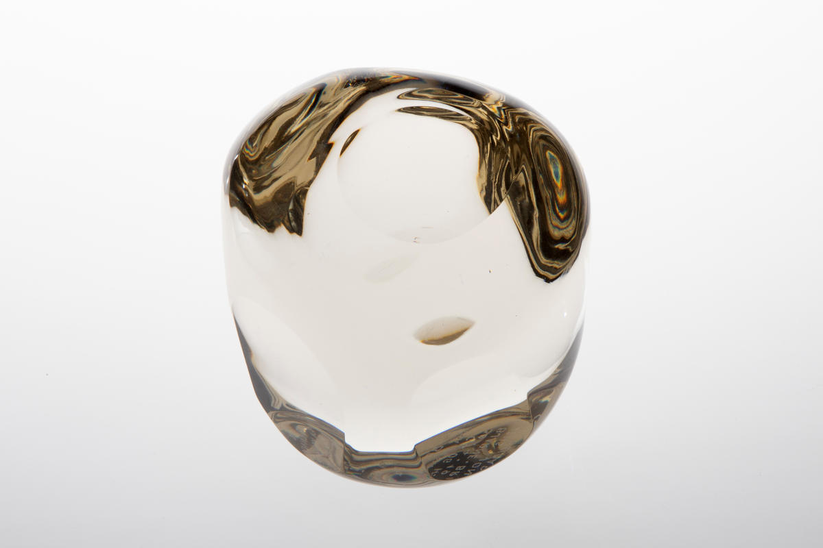 Irregulær kuleformet skulptur av massiv klart glass med slipte ovalformede og runde partier på yttersiden.