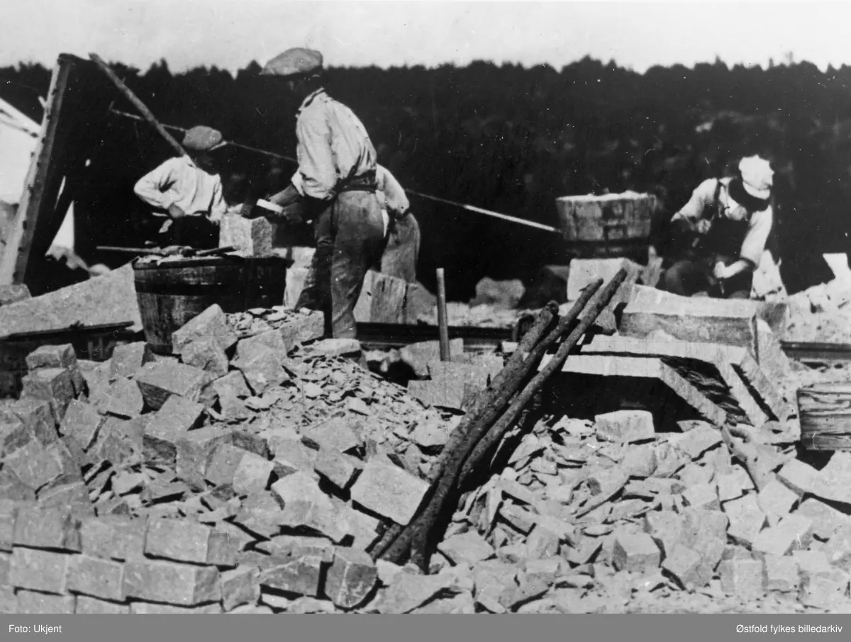 Huggeplassen i stenbrudd - storbruddet på Greåke i Tune 1920. Utsnitt: Fire stenhoggere bearbeider sten i storbruddet på Greåker.
Krana på kanten av "Høla". Produksjon av småsten (gatesten/kantsten)