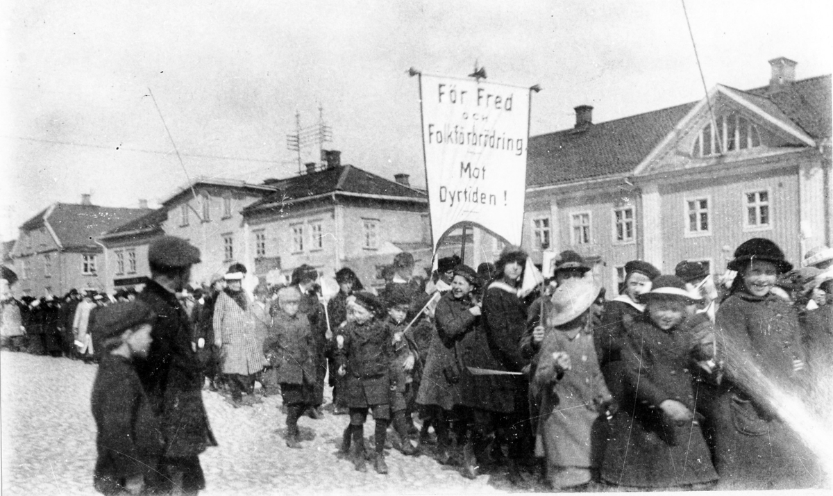 Demonstrationståg i och med första maj under första världskriget, troligen 1918. En fana med text: "För fred och förbrödring i dyrtiden". Tåget går förbi på Stora torget.