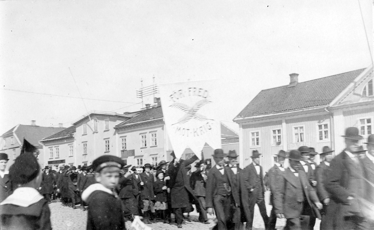 Demonstrationståg i och med första maj under första världskriget. En fana med text: "För fred mot krig". Tåget går förbi på Stora torget.