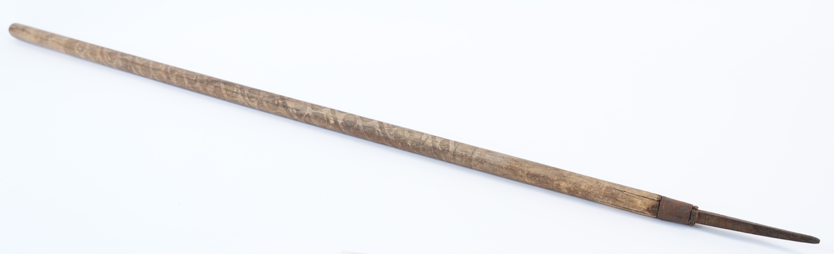 Treskurd i den store sentrale delen av staven. Dekorasjonen begynner under plass for handa (18 cm ovanfrå) og ender i ei høgde på 44 cm. Den heile hovuddelen med bladrankar i spiral er strekt mellom to striper med fiskebeinsmønstra (1 oppe, 1 nede). Jernbeslaga også med dekorasjon: jernholken med bord av to fletter, piggen med fire voluttar oppe og krysskors og inskripsjon på sidene.