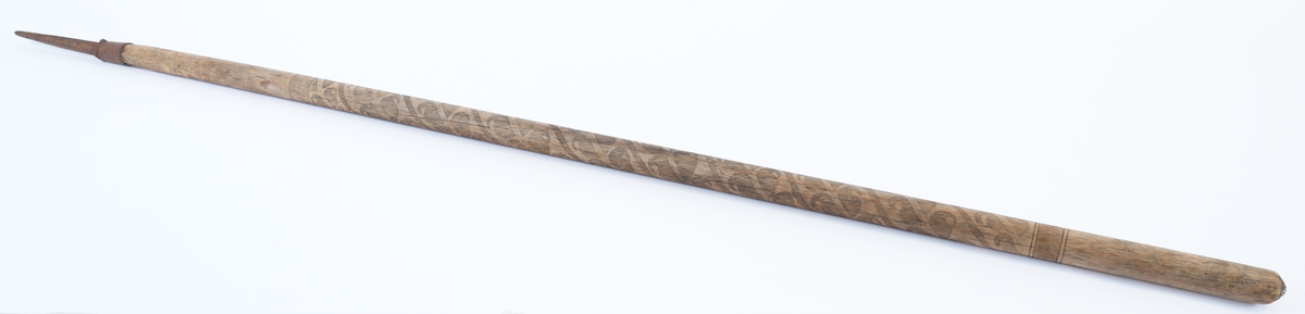 Treskurd i den store sentrale delen av staven. Dekorasjonen begynner under plass for handa (18 cm ovanfrå) og ender i ei høgde på 44 cm. Den heile hovuddelen med bladrankar i spiral er strekt mellom to striper med fiskebeinsmønstra (1 oppe, 1 nede). Jernbeslaga også med dekorasjon: jernholken med bord av to fletter, piggen med fire voluttar oppe og krysskors og inskripsjon på sidene.