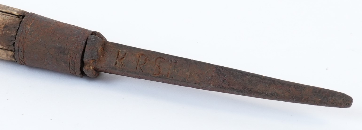 Treskurd i den store sentrale delen av staven. Dekorasjonen begynner under plass for handa (18 cm ovanfrå) og ender i ei høgde på 44 cm. Den heile hovuddelen med bladrankar i spiral er strekt mellom to striper med fiskebeinsmønstra (1 oppe, 1 nede). Jernbeslaga også med dekorasjon: jernholken med bord av to fletter, piggen med fire voluttar oppe og krysskors og inskripsjon på sidene.