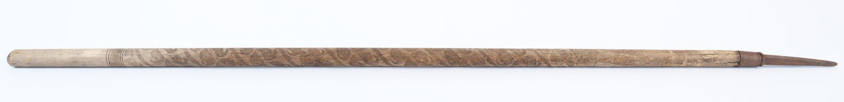 Treskurd i den store sentrale delen av staven. Dekorasjonen begynner under plass for handa (18 cm ovanfrå) og ender i ei høgde på 44 cm. Den heile hovuddelen med bladrankar i spiral er strekt mellom to striper med fiskebeinsmønstra (1 oppe, 1 nede). Jernbeslaga også med dekorasjon: jernholken med bord av to fletter, piggen med fire voluttar oppe og krysskors og inskripsjon på sidene.
