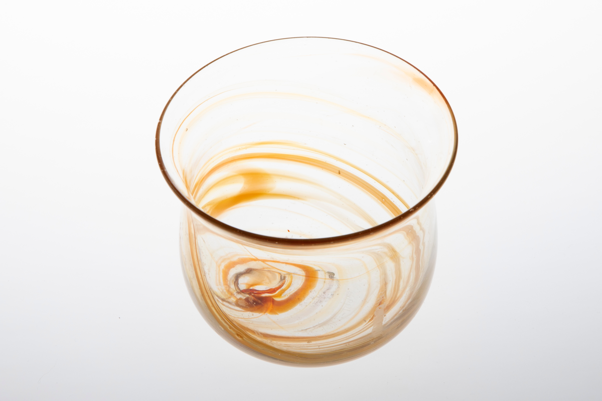 Glassbolle i klart glass. Bollen har kuleformet korpus med utoverbrettet munningsrand. I det klare glasset er det rød- og oransjefargde partier som slynger seg rundt korpus.