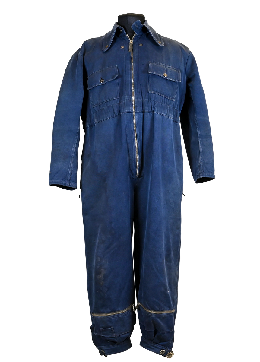 Mekanikeroverall i blå denim från Östgöta flygfottilj, F3. Overallen har två bröstfickor med lock som försluts med metallknapp. Längs ner vid fotändarna sitter en mindre ficka på vardera ben som sluts med dragkedja. På vardera sida vid midjan sitter fickor med dragkedja och löpare i skinn. På baksidan finns en bakficka på höger ben. Overallen har en krage som går att vika upp och stänga med två tygband och metallknappar. Den yttersta knappen på rad två av knappar sitter löst, Kragen går att vika ner och fästa i overallen med tryckknappar i metall. På insidan av midjan sitter en dragsko. Fotändarna kan spännas med en skinnrem. Overallen stängs med dragkedja i metall. 

På plaggets insida finns ett vitt tryck med texten "F3 2". F3 talar om att overallen användes vid Östgöta flygfottilj. 2:an anger troligtvis storleken på plagget.

Overallen har fyra stycken lagningar nere på höger baksida.