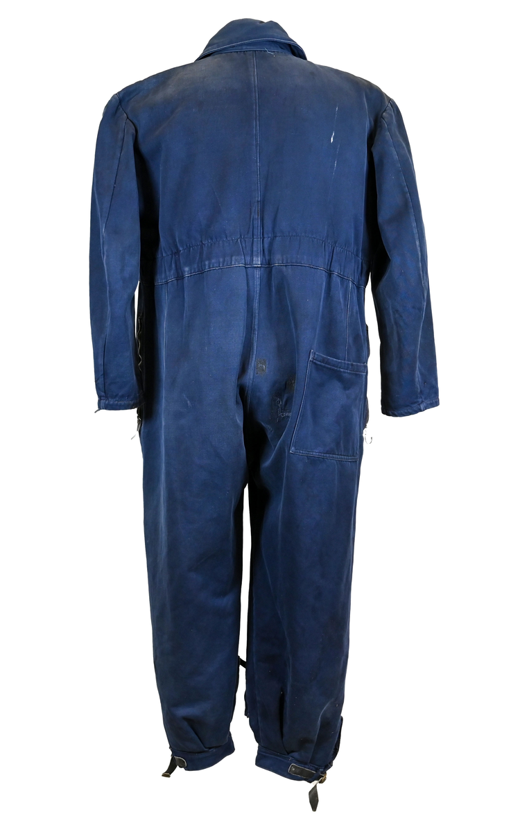 Mekanikeroverall i blå denim från Östgöta flygfottilj, F3. Overallen har två bröstfickor med lock som försluts med metallknapp. Längs ner vid fotändarna sitter en mindre ficka på vardera ben som sluts med dragkedja. På vardera sida vid midjan sitter fickor med dragkedja och löpare i skinn. På baksidan finns en bakficka på höger ben. Overallen har en krage som går att vika upp och stänga med två tygband och metallknappar. Den yttersta knappen på rad två av knappar sitter löst, Kragen går att vika ner och fästa i overallen med tryckknappar i metall. På insidan av midjan sitter en dragsko. Fotändarna kan spännas med en skinnrem. Overallen stängs med dragkedja i metall. 

På plaggets insida finns ett vitt tryck med texten "F3 2". F3 talar om att overallen användes vid Östgöta flygfottilj. 2:an anger troligtvis storleken på plagget.

Overallen har fyra stycken lagningar nere på höger baksida.