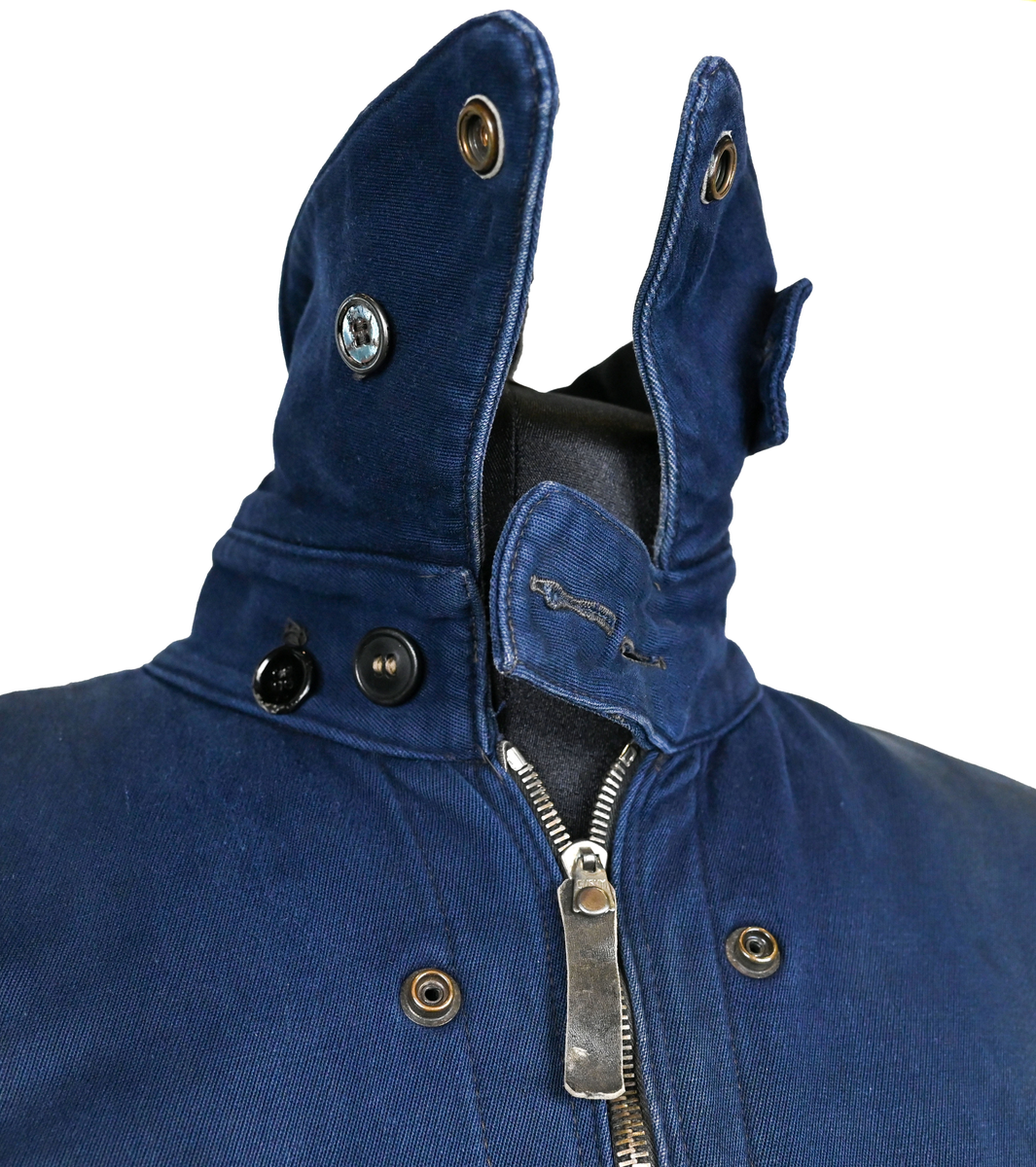 Mekanikeroverall i blå denim från Östgöta flygfottilj, F3. Overallen har två bröstfickor med lock som försluts med metallknapp. Längs ner vid fotändarna sitter en mindre ficka på vardera ben som sluts med dragkedja. På vardera sida vid midjan sitter fickor med dragkedja och löpare i skinn. På baksidan finns en bakficka på höger ben. Overallen har en krage som går att vika upp och stänga med två tygband och metallknappar. Den yttersta knappen på rad två av knappar sitter löst, Kragen går att vika ner och fästa i overallen med tryckknappar i metall. På insidan av midjan sitter en dragsko. Fotändarna kan spännas med en skinnrem. Overallen stängs med dragkedja i metall. 

På plaggets insida finns ett vitt tryck med texten "F3 2". F3 talar om att overallen användes vid Östgöta flygfottilj. 2:an anger troligtvis storleken på plagget.

Overallen har fyra stycken lagningar nere på höger baksida.