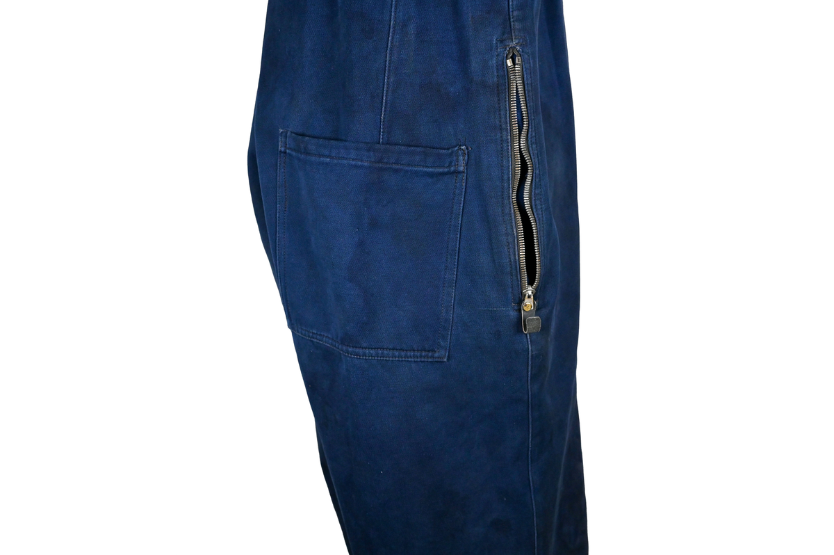 Mekanikeroverall i blå denim från Östgöta flygfottilj, F3. Overallen har två bröstfickor med lock som försluts med metallknapp. Längs ner vid fotändarna sitter en mindre ficka på vardera ben som sluts med dragkedja. På vardera sida vid midjan sitter fickor med dragkedja och löpare i skinn. På baksidan finns en bakficka på höger ben. Overallen har en krage som går att vika upp och stänga med två tygband och metallknappar. Den yttersta knappen på rad två av knappar sitter löst, Kragen går att vika ner och fästa i overallen med tryckknappar i metall. På insidan av midjan sitter en dragsko. Fotändarna kan spännas med en skinnrem. Overallen stängs med dragkedja i metall. 

På plaggets insida finns ett vitt tryck med texten "F3 2". F3 talar om att overallen användes vid Östgöta flygfottilj. 2:an anger troligtvis storleken på plagget.

Overallen har fyra stycken lagningar nere på höger baksida.