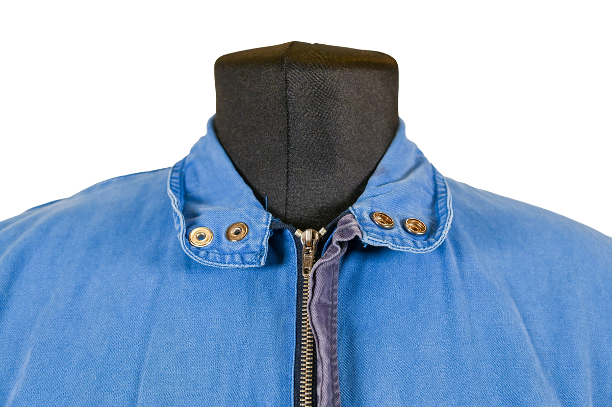 Blå arbetsoverall från SAS AB. På plagget finns en logga för SAS över vänster bröst och mitt på ryggen. Overallen har två bröstfickor med reflexband som försluts med kardborre. På framsidan under midjan sitter två större framfickor med lock och på vardera ben sitter ytterligare två fickor på sidorna. På baksidan finns två stora bakfickor. Högt upp på höger ärm sitter ytterligare en ficka av genomskinlig plast. Samtliga fickor försluts med kardborre förutom bakfickorna som stängs med plastknapp. Förutom på bröstfickorna sitter även reflexband runt benens nedre del samt högt upp över ryggen. Overallen sluts med dragkedja och två tryckknappar i metall på kragen. Vid höfterna finns två öppningar in i overallen. På knäna finns öppningar för att lägga i knäskydd.

Overallen är producerad av Fristads i storlek 50C. På lappen i nacken finns utrymme för namnteckning. På insidan av overallen vid midjan sitter en nött lapp som inte längre har någon information.

Plaggets framsida är befläckad med vit färg. Fotändar och ärmar är nötta. Flertalet mindre hål i höger ärm samt början till hål på vänster ärm.