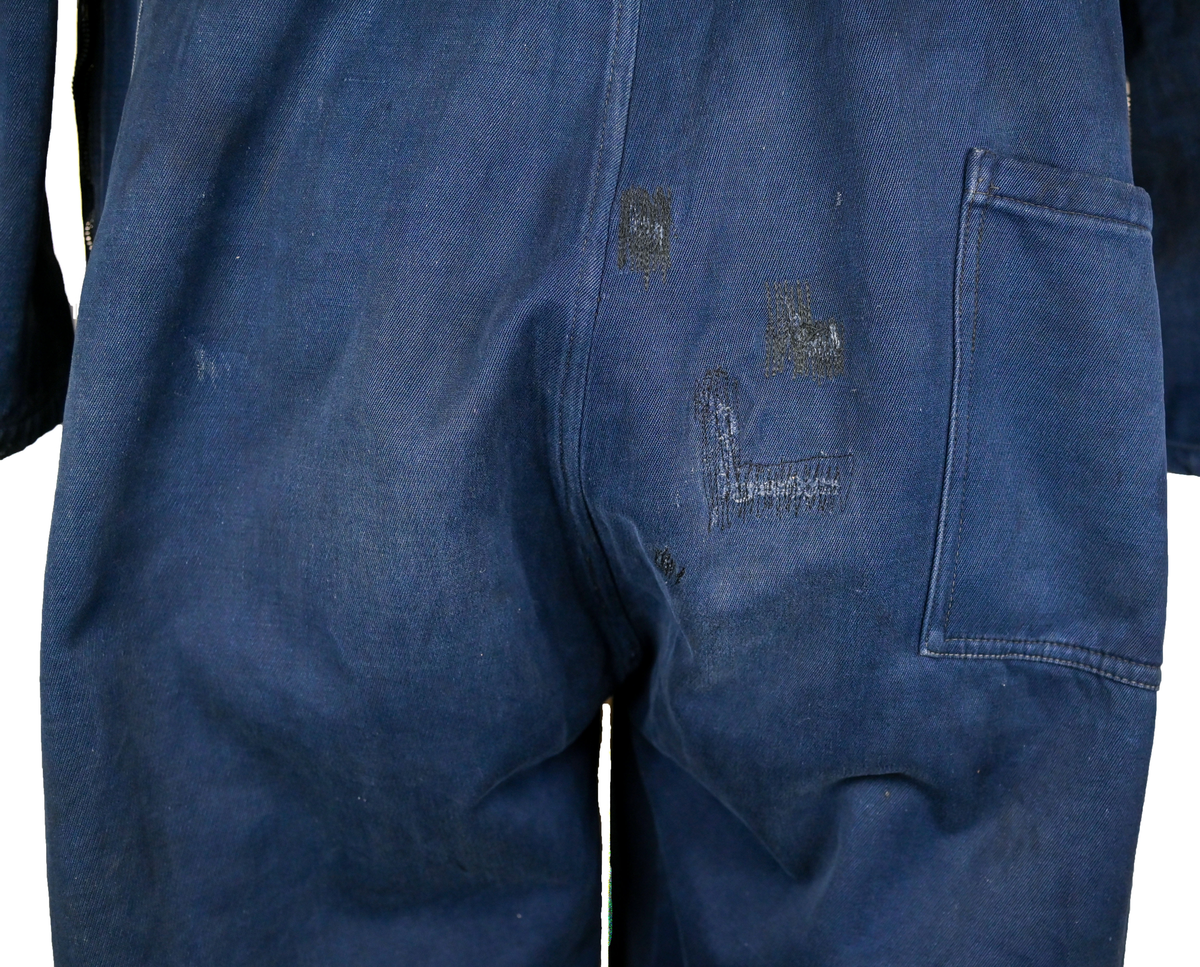 Mekanikeroverall i blå denim från Östgöta flygfottilj, F3. Overallen har två bröstfickor med lock som försluts med metallknapp. Längs ner vid fotändarna sitter en mindre ficka på vardera ben som sluts med dragkedja. På vardera sida vid midjan sitter fickor med dragkedja och löpare i skinn. På baksidan finns en bakficka på höger ben. Overallen har en krage som går att vika upp och stänga med två tygband och metallknappar. Den yttersta knappen på rad två av knappar sitter löst, Kragen går att vika ner och fästa i overallen med tryckknappar i metall. På insidan av midjan sitter en dragsko. Fotändarna kan spännas med en skinnrem. Overallen stängs med dragkedja i metall. 

På plaggets insida finns ett vitt tryck med texten "F3 2". F3 talar om att overallen användes vid Östgöta flygfottilj. 2:an anger troligtvis storleken på plagget.

Overallen har fyra stycken lagningar nere på höger baksida.