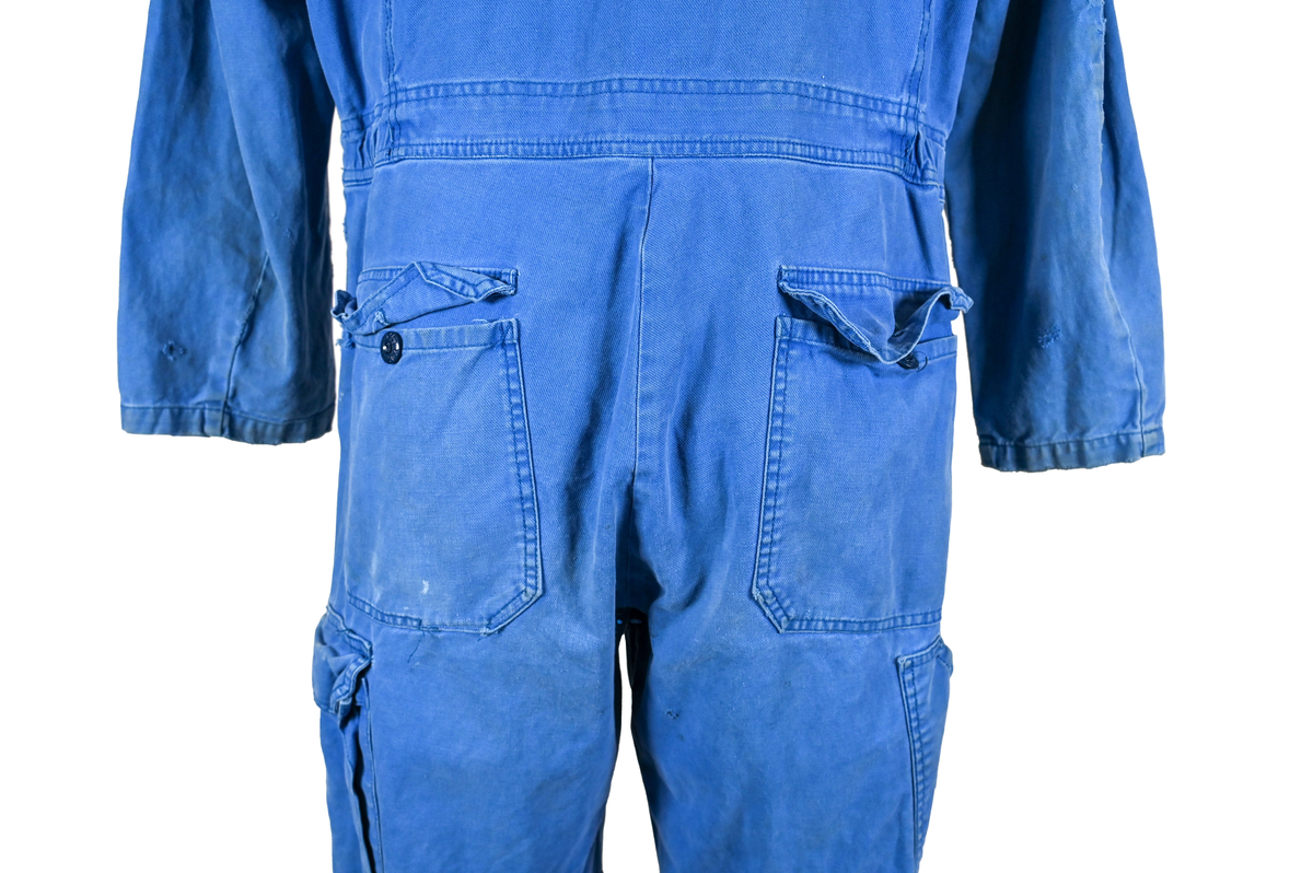 Blå arbetsoverall från SAS AB. På plagget finns en logga för SAS över vänster bröst och mitt på ryggen. Overallen har två bröstfickor med reflexband som försluts med kardborre. På framsidan under midjan sitter två större framfickor med lock och på vardera ben sitter ytterligare två fickor på sidorna. På baksidan finns två stora bakfickor. Högt upp på höger ärm sitter ytterligare en ficka av genomskinlig plast. Samtliga fickor försluts med kardborre förutom bakfickorna som stängs med plastknapp. Förutom på bröstfickorna sitter även reflexband runt benens nedre del samt högt upp över ryggen. Overallen sluts med dragkedja och två tryckknappar i metall på kragen. Vid höfterna finns två öppningar in i overallen. På knäna finns öppningar för att lägga i knäskydd.

Overallen är producerad av Fristads i storlek 50C. På lappen i nacken finns utrymme för namnteckning. På insidan av overallen vid midjan sitter en nött lapp som inte längre har någon information.

Plaggets framsida är befläckad med vit färg. Fotändar och ärmar är nötta. Flertalet mindre hål i höger ärm samt början till hål på vänster ärm.