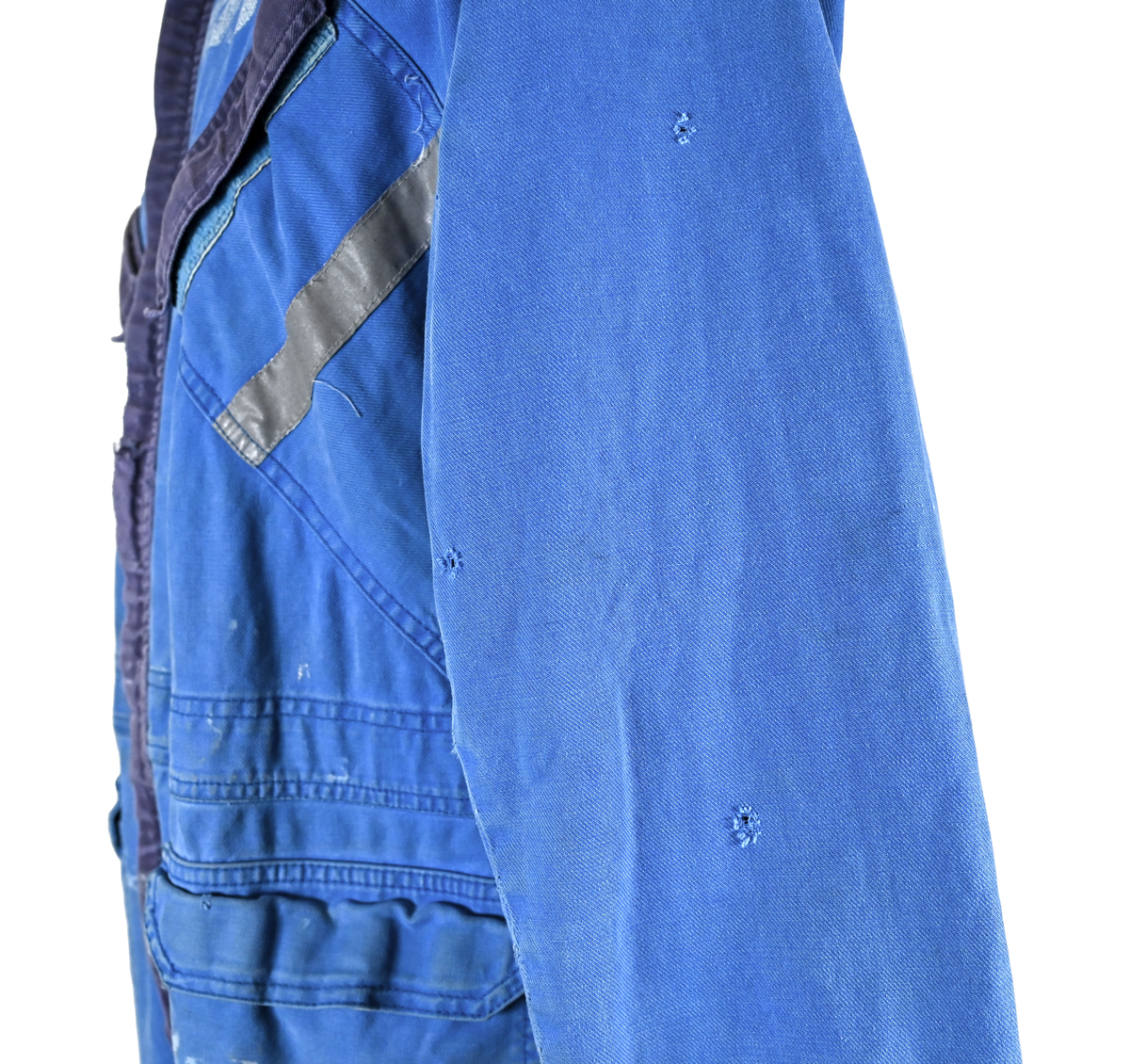 Blå arbetsoverall från SAS AB. På plagget finns en logga för SAS över vänster bröst och mitt på ryggen. Overallen har två bröstfickor med reflexband som försluts med kardborre. På framsidan under midjan sitter två större framfickor med lock och på vardera ben sitter ytterligare två fickor på sidorna. På baksidan finns två stora bakfickor. Högt upp på höger ärm sitter ytterligare en ficka av genomskinlig plast. Samtliga fickor försluts med kardborre förutom bakfickorna som stängs med plastknapp. Förutom på bröstfickorna sitter även reflexband runt benens nedre del samt högt upp över ryggen. Overallen sluts med dragkedja och två tryckknappar i metall på kragen. Vid höfterna finns två öppningar in i overallen. På knäna finns öppningar för att lägga i knäskydd.

Overallen är producerad av Fristads i storlek 50C. På lappen i nacken finns utrymme för namnteckning. På insidan av overallen vid midjan sitter en nött lapp som inte längre har någon information.

Plaggets framsida är befläckad med vit färg. Fotändar och ärmar är nötta. Flertalet mindre hål i höger ärm samt början till hål på vänster ärm.