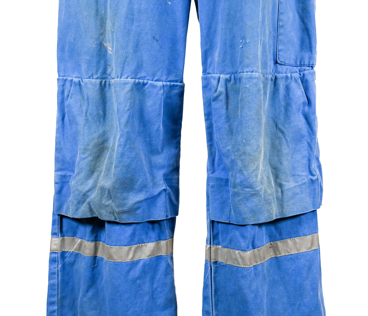 Blå arbetsoverall från SAS AB. På plagget finns en logga för SAS över vänster bröst och mitt på ryggen. Overallen har två bröstfickor med reflexband som försluts med kardborre. På framsidan under midjan sitter två större framfickor med lock och på vardera ben sitter ytterligare två fickor på sidorna. På baksidan finns två stora bakfickor. Högt upp på höger ärm sitter ytterligare en ficka av genomskinlig plast. Samtliga fickor försluts med kardborre förutom bakfickorna som stängs med plastknapp. Förutom på bröstfickorna sitter även reflexband runt benens nedre del samt högt upp över ryggen. Overallen sluts med dragkedja och två tryckknappar i metall på kragen. Vid höfterna finns två öppningar in i overallen. På knäna finns öppningar för att lägga i knäskydd.

Overallen är producerad av Fristads i storlek 50C. På lappen i nacken finns utrymme för namnteckning. På insidan av overallen vid midjan sitter en nött lapp som inte längre har någon information.

Plaggets framsida är befläckad med vit färg. Fotändar och ärmar är nötta. Flertalet mindre hål i höger ärm samt början till hål på vänster ärm.