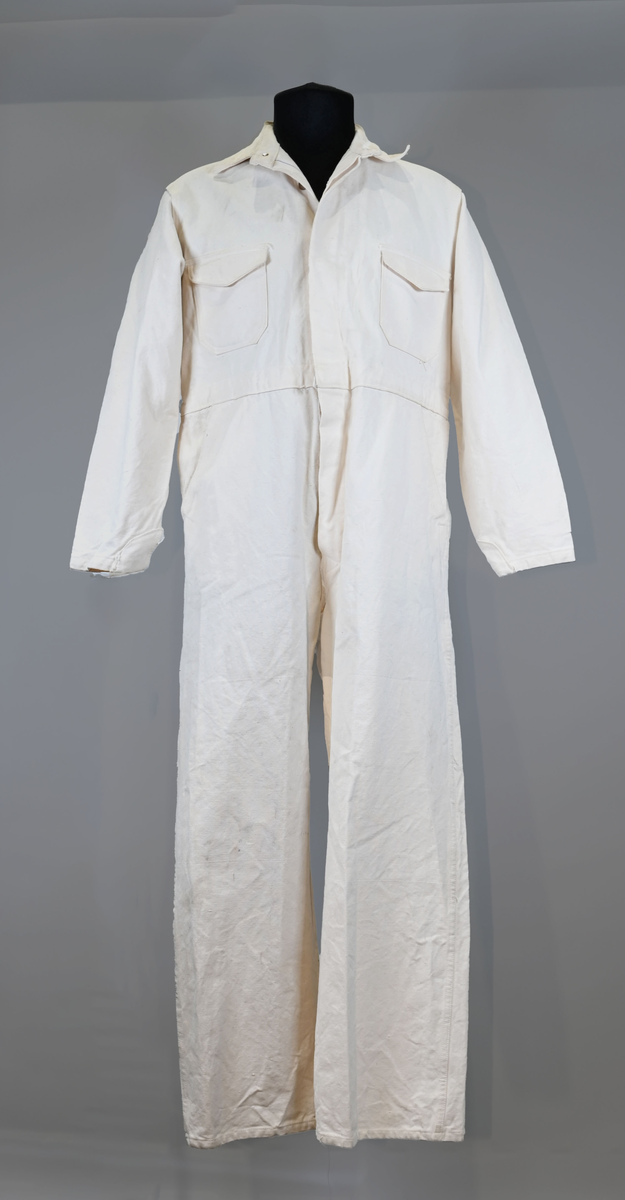 Arbetsoverall i vitt, grövre tyg för personal vid AB Aerotransport. På ryggen finns ett tryck i mörkgrå färg föreställande företagets logga och initialer, ABA. Overallen har två bröstfickor på vardera sida samt två fram- och bakfickor. Under bakfickan på höger ben sitter ytterligare en mindre ficka. Overallen har krage och mässingsfärgade metallknappar. Plagget är utsatt för visst slitage och smuts.