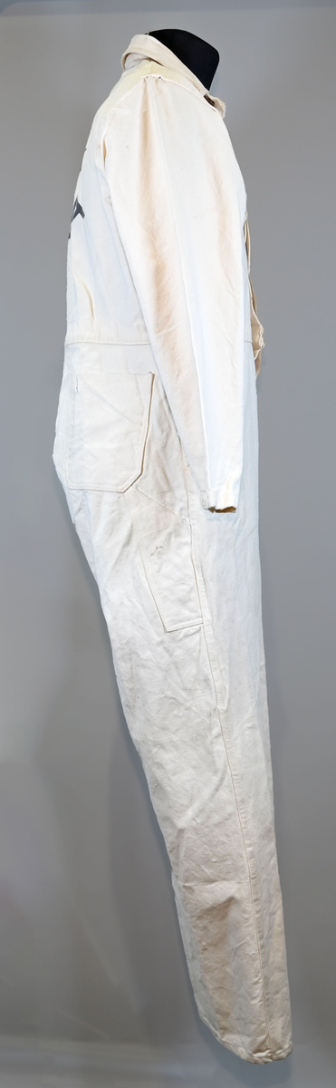 Arbetsoverall i vitt, grövre tyg för personal vid AB Aerotransport. På ryggen finns ett tryck i mörkgrå färg föreställande företagets logga och initialer, ABA. Overallen har två bröstfickor på vardera sida samt två fram- och bakfickor. Under bakfickan på höger ben sitter ytterligare en mindre ficka. Overallen har krage och mässingsfärgade metallknappar. Plagget är utsatt för visst slitage och smuts.