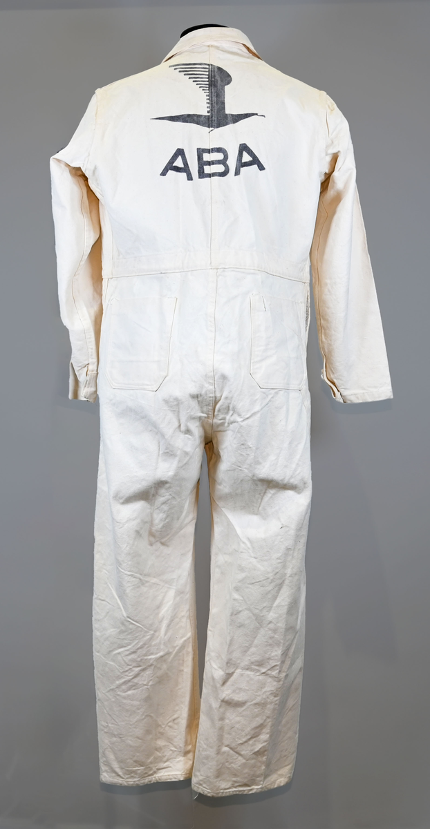 Arbetsoverall i vitt, grövre tyg för personal vid AB Aerotransport. På ryggen finns ett tryck i mörkgrå färg föreställande företagets logga och initialer, ABA. Overallen har två bröstfickor på vardera sida samt två fram- och bakfickor. Under bakfickan på höger ben sitter ytterligare en mindre ficka. Overallen har krage och mässingsfärgade metallknappar. Plagget är utsatt för visst slitage och smuts.
